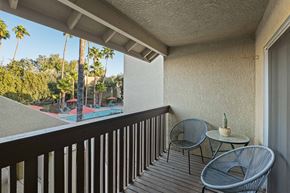 Tucson apartment for rent - A balcony with a table and two chairs overlooking a pool and palm trees.