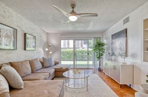 Austin apartment for rent - Spacious living room with brown concrete floors, white brick walls, popcorn ceiling, ceiling fan, and a sliding glass door to a patio