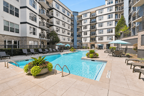 Atlanta apartment for rent - A large swimming pool surrounded by lounge chairs and umbrellas in a courtyard.