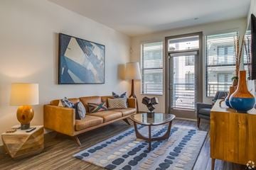 Tempe apartment for rent - A living room with a brown couch, a blue rug, and a painting on the wall.