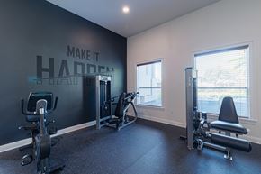 Houston apartment for rent - A gym with a wall that says "make it happen" and a row of exercise equipment.