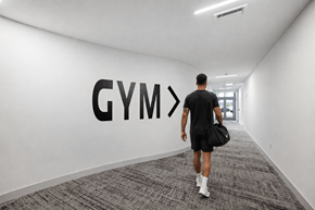Miami apartment for rent - A man walking in a hallway with a Gym sign on the wall.