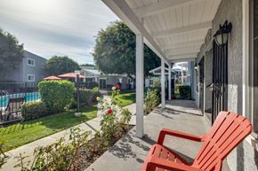 Oceanside apartment for rent - A red chair sits on a patio with a pool and trees in the background.
