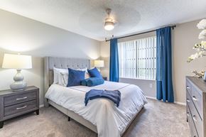 North Lauderdale apartment for rent - A bedroom with a large bed, a nightstand, and a window with blue curtains.