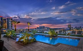 Phoenix apartment for rent - A rooftop pool with palm trees and a city skyline at dusk.