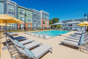 Charlotte apartment for rent - A pool area with sun loungers and umbrellas in front of apartment buildings.