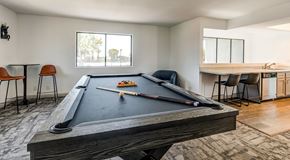 Ontario apartment for rent - A pool table with a billiard cue and balls is in the foreground of a room with a dining table and chairs in the background.
