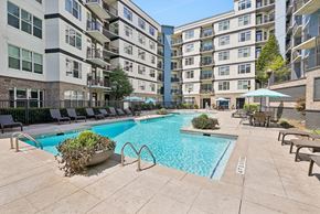 Atlanta apartment for rent - A large swimming pool surrounded by lounge chairs and umbrellas in a courtyard with apartment buildings in the background.