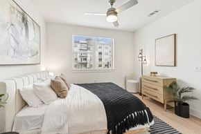 San Antonio apartment for rent - A bedroom with a large bed, a ceiling fan, and a window with a view of a building outside.