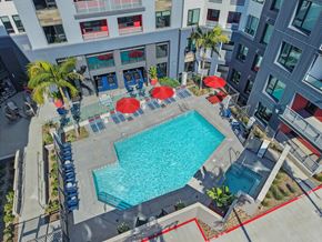 Oxnard apartment for rent - A swimming pool surrounded by red umbrellas and blue chairs.