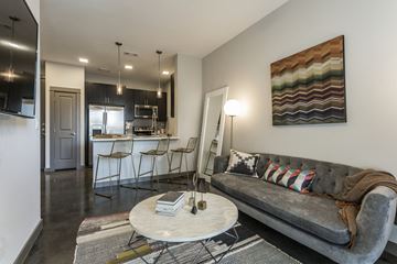 Houston apartment for rent - A grey couch with a blanket on it sits in a living room with a white coffee table in front of it.
