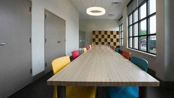A long wooden table is surrounded by colorful chairs in a room with a checkerboard patterned wall.