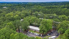 Cary apartment for rent - A parking lot with cars and a building surrounded by trees. at Arbors at Cary, Cary, 27511