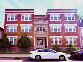 Roxbury apartment for rent - A white car is parked in front of a red brick building.