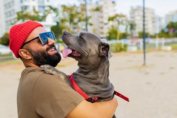 A man in a red beanie and sunglasses is holding a dog on a leash.