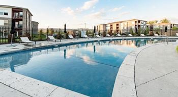 A large outdoor swimming pool with lounge chairs and a fence around it.