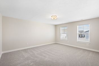 A room with a carpeted floor and two windows.