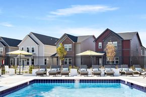 Brownsburg apartment for rent - A pool area with lounge chairs and umbrellas in front of a row of houses.