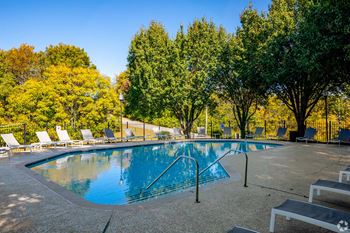 A swimming pool with chairs around it and trees in the background