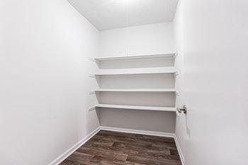 A walk in closet with white shelves and a wood floor