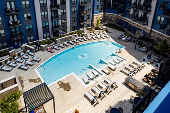 A large swimming pool with chaise lounge chairs and an apartment building in the background