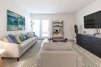 A living room with a beige couch, a grey ottoman, and a painting on the wall.