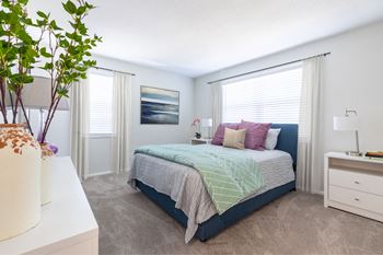 A bedroom with a bed, nightstand, and a plant.