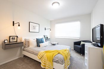 A bedroom with a bed, a nightstand, a chair, and a television.