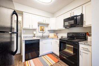 A black fridge is in the corner of a kitchen with white cabinets.