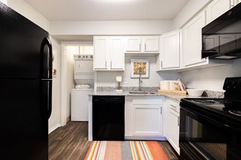 A black refrigerator is on the left in a kitchen with white cabinets.