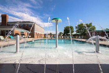 A water fountain in the middle of a pool surrounded by buildings.
