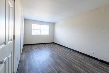 The living room of an empty apartment with wood flooring and a window