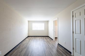 The living room of an empty house with wood floors and a window