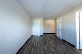 The living room of an empty apartment with wood flooring and a door
