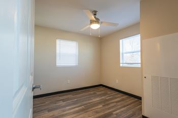 An empty room with a ceiling fan and two windows