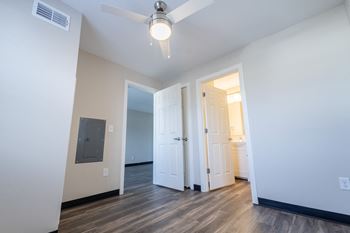 A bedroom with white walls and wood flooring and a door to a bathroom
