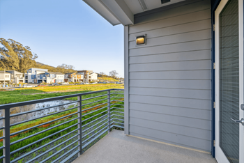 A grey house with a balcony overlooking a grassy area.