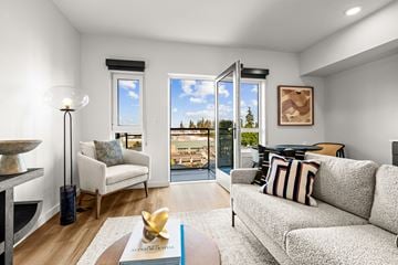 Shoreline apartment for rent - A living room with a grey couch, a white chair, a table with a book and a gold object on it, and a view of the outside through the windows.