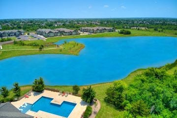 Oklahoma City apartment for rent - A large blue swimming pool surrounded by a grassy area and a residential neighborhood in the background.