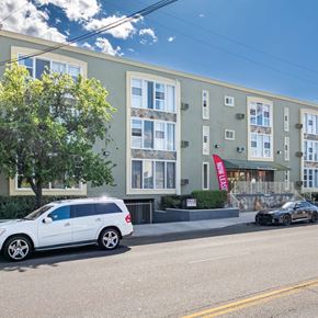 Sherman Oaks apartment for rent - A white car is parked in front of a green building with a tree to the left.