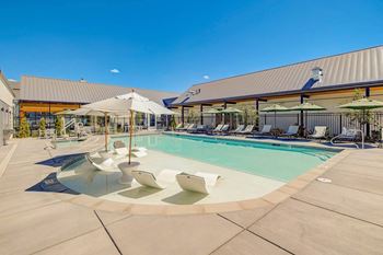 A pool with lounge chairs and umbrellas in front of a building