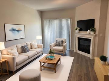 Sacramento apartment for rent - A living room with a white couch, a grey ottoman, a wooden coffee table, a fireplace, and a painting on the wall.