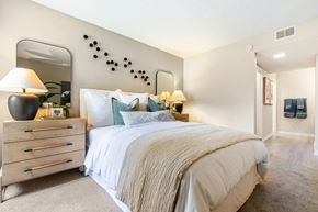 Cypress apartment for rent - A bedroom with a large bed, a dresser with a lamp, and a mirror on the wall.