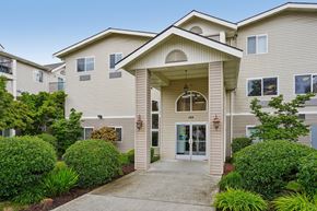 Burien apartment for rent - A beige building with a front entrance and bushes.