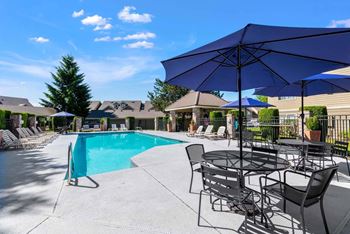 A pool area with a table and chairs and umbrellas.