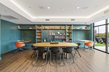 A room with a round table surrounded by chairs and a bookshelf filled with books.