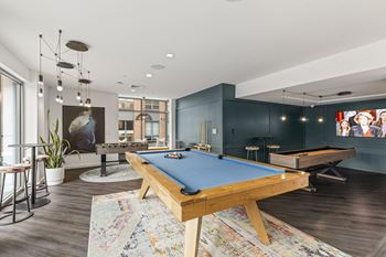 A pool table is in the middle of a room with a bar stool and a potted plant.
