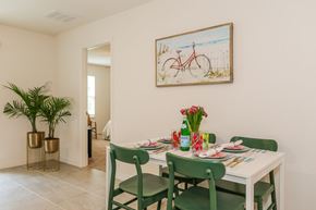 Jacksonville townhouse for rent - Dining room with a white table set for four, green chairs, tropical plants, and beach-themed artwork.