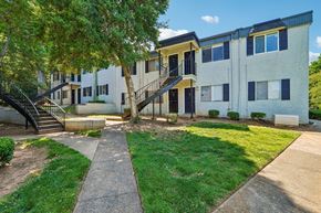 Charlotte apartment for rent - A concrete pathway leads to a building with a tree in front.