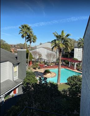 Houston apartment for rent - A pool surrounded by palm trees and a red roof.